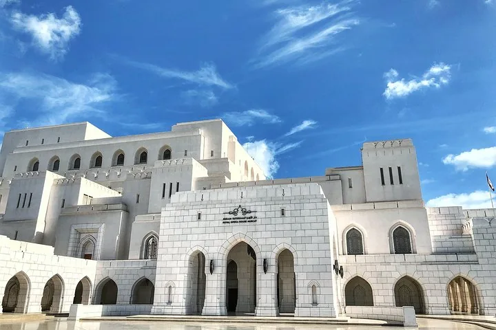 Het opvallende witte exterieur van het Royal Opera House Muscat tegen een blauwe lucht.