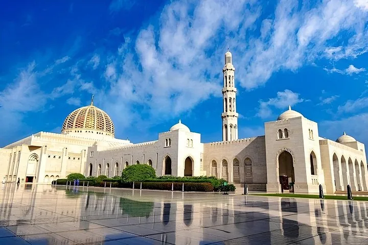 Brede foto van de uitgestrekte Sultan Qaboos Grand Mosque die weerspiegelt in de gepolijste binnenplaats.